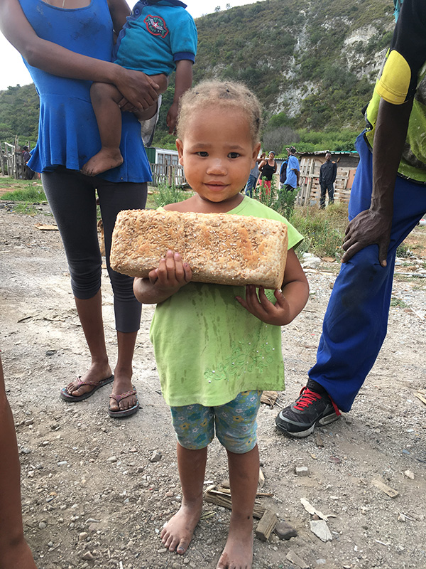 Klein kind houdt trots een versgebakken brood vast in Port Elisabeth, Zuid-Afrika, bij een project van The Breadhouse dat lokale bakkerijen ondersteunt.