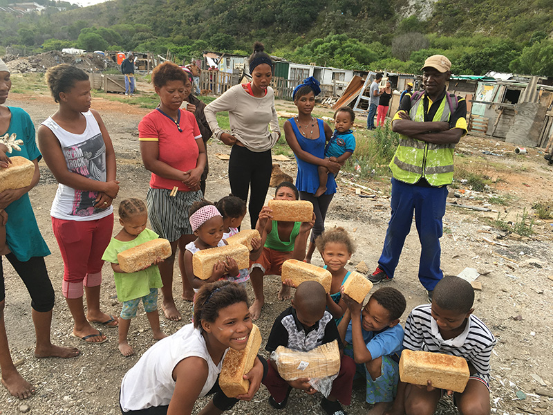 Groep kinderen en volwassenen in een Zuid-Afrikaanse nederzetting toont trots versgebakken broden die zij hebben ontvangen van The Breadhouse.
